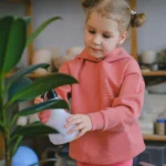 A young girl watering an indoor plant.